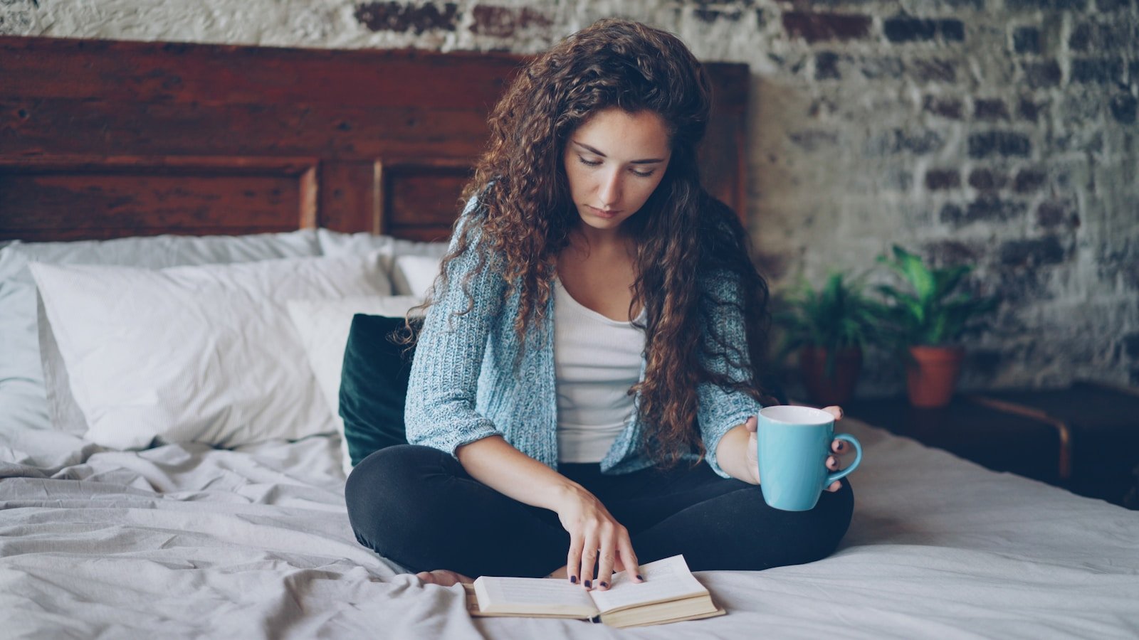 Young woman reading a book on a bed with coffee.